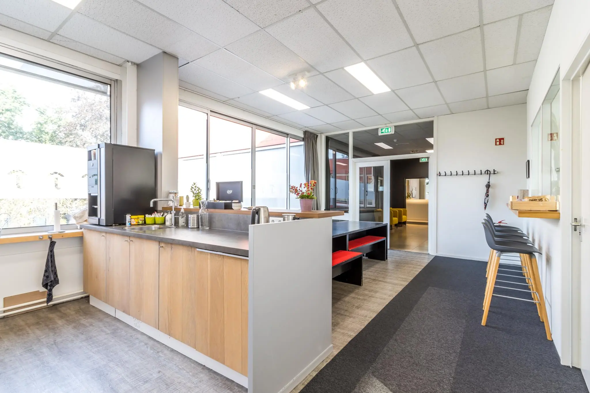 Moderne kantine met houten keuken, zitbanken met rode kussens en barkrukken in een kantoor aan de Jan van Eycklaan.